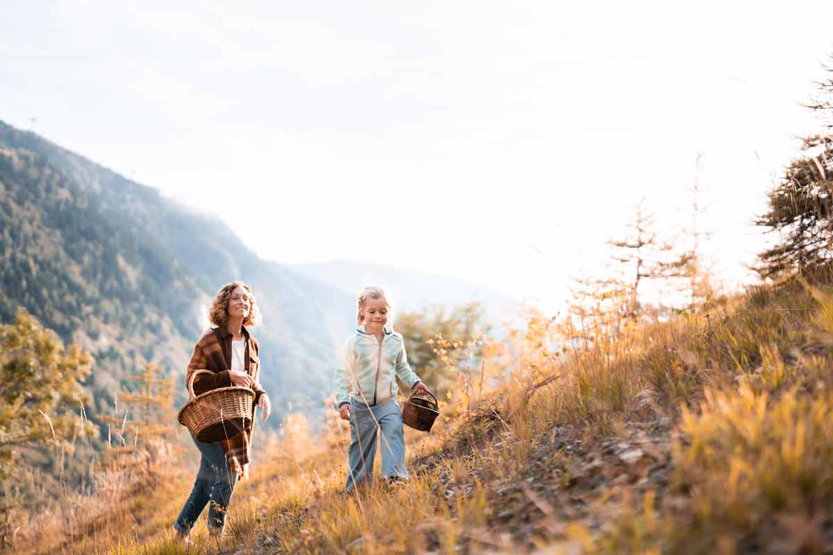 Maman et sa fille marchant avec des paniers sur une pente montagneuse aux couleurs d'automne dans une douce lumière