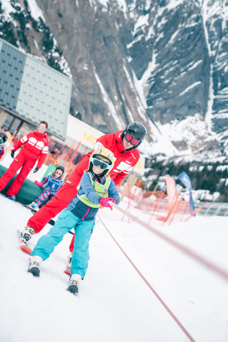 Enfant sur un fil neige apprenant le ski avec un moniteur de ski ESF
