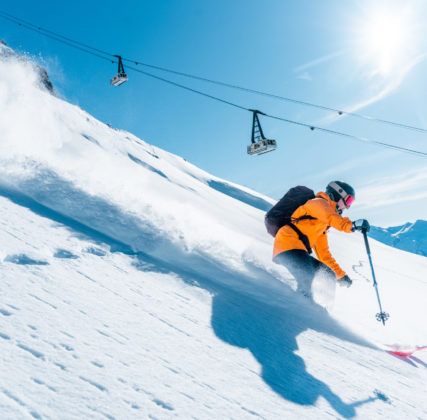 Skieur dans la neige fraiche en premier plan et téléphérique en arrière plan