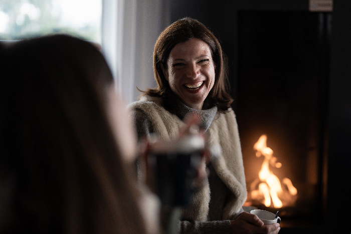 Femme souriante dans un intérieur avec feu de cheminée en arrière plan.